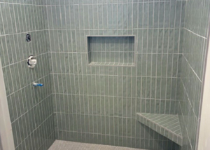 Shower tile design featuring sage green vertical subway tiles and built-in corner bench.